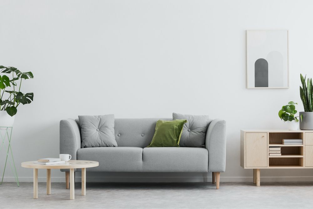 Living room with gray sofa, green and gray pillows, round coffee table, and wood cabinet with plant.