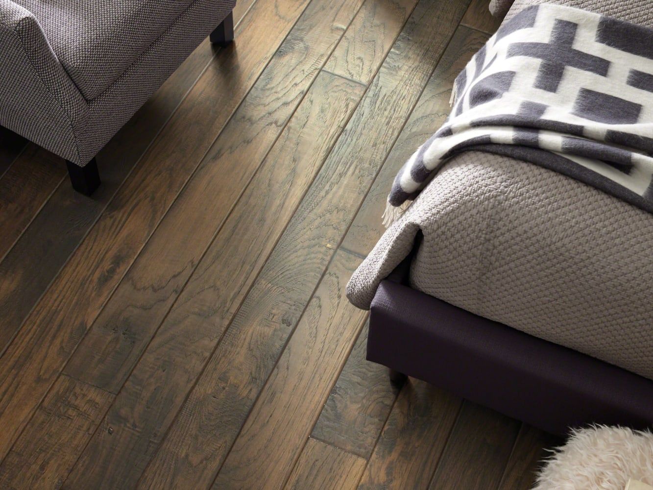 Hardwood floor with a bed and armchair; flooring is dark brown, furnishings are muted.