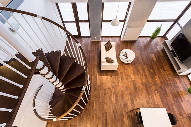 High-angle view of a modern living space with a spiral staircase, wooden floors, and large windows.