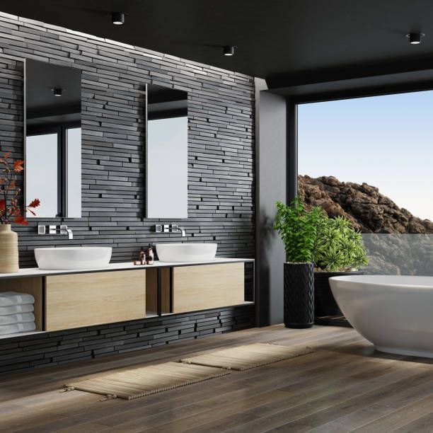 Modern bathroom with stone wall, wooden vanity, mirrors, tub, and window overlooking landscape.