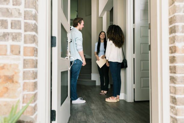 People talking inside a home's entryway; open doorway, man and two women, one with documents.
