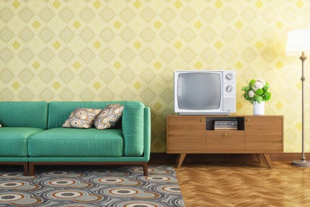 Green sofa, vintage TV, and wooden cabinet against yellow patterned wallpaper.