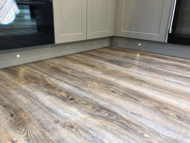 Kitchen floor with wood-look laminate and grey cabinets. Under-cabinet lighting illuminates the corner.