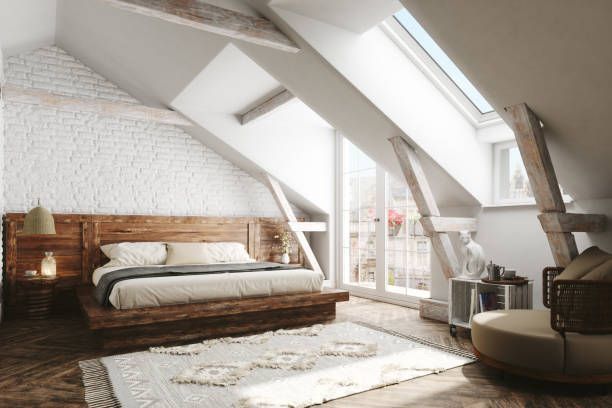 Bedroom in a white-walled attic with a large wooden bed, window, and decorative rug.