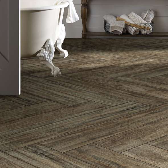 Herringbone patterned brown wood-look tile floor in a bathroom with a claw-foot tub and folded towels.