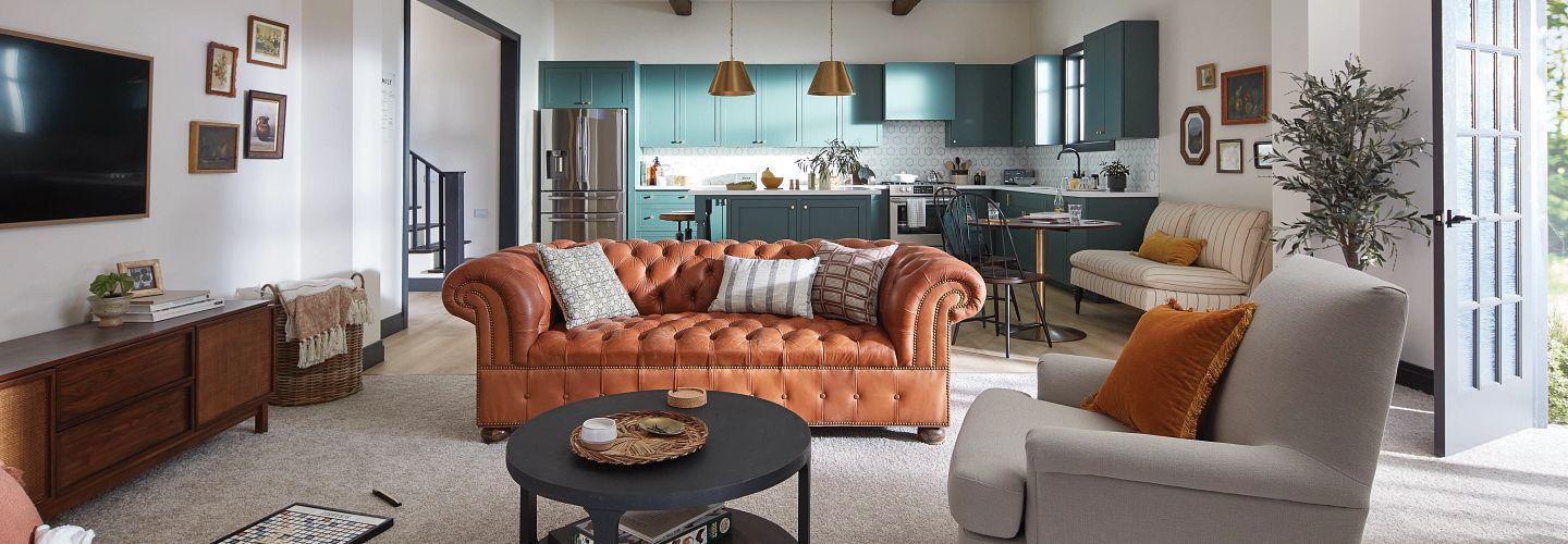 Living room with orange leather sofa, teal kitchen cabinets, and light gray armchair.