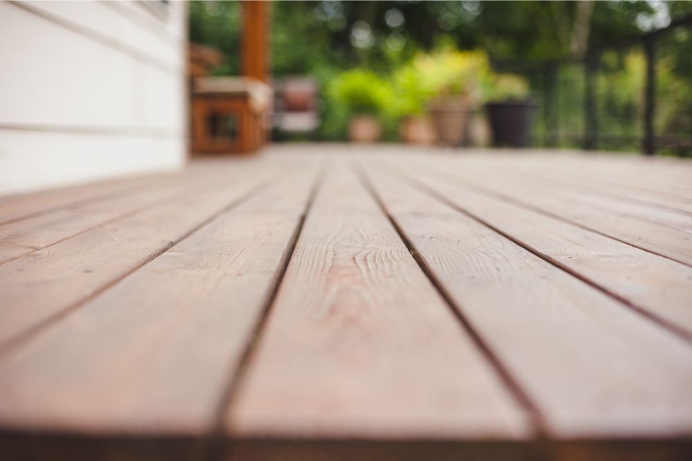 Wooden deck with a blurred background of greenery and a house.