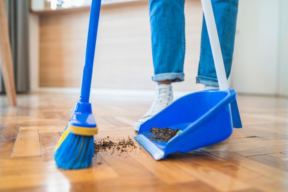 Person sweeping wooden floor with blue broom and dustpan.
