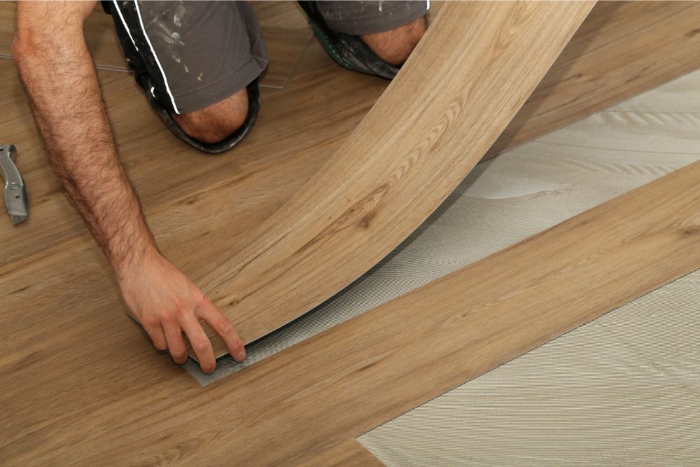 Person installing wood-look flooring, bending a plank into place over an underlayment.