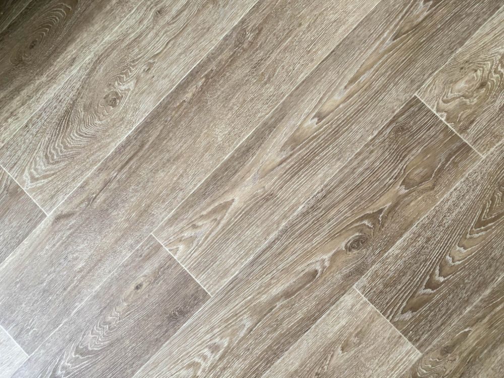 Diagonal view of light brown wood-look flooring with visible grain and rectangular tiles.