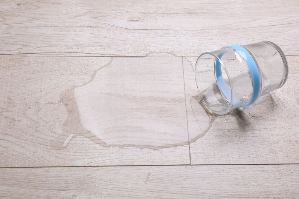 Spilled water on wooden floor; glass with blue ring overturned.