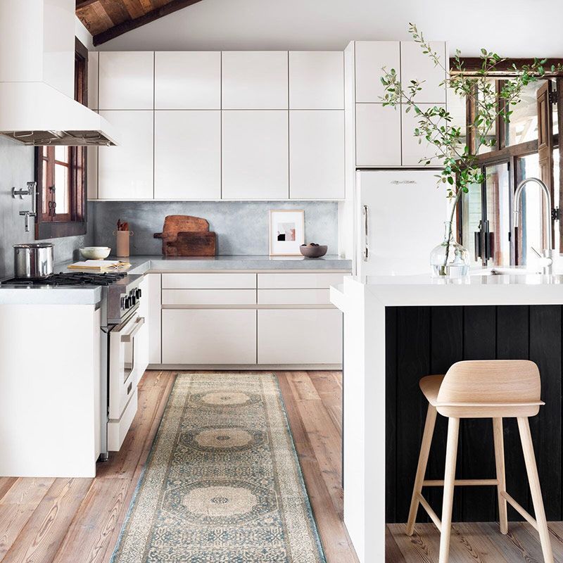 White kitchen with light wood floors, a patterned rug, and a black accent wall with a wooden stool.
