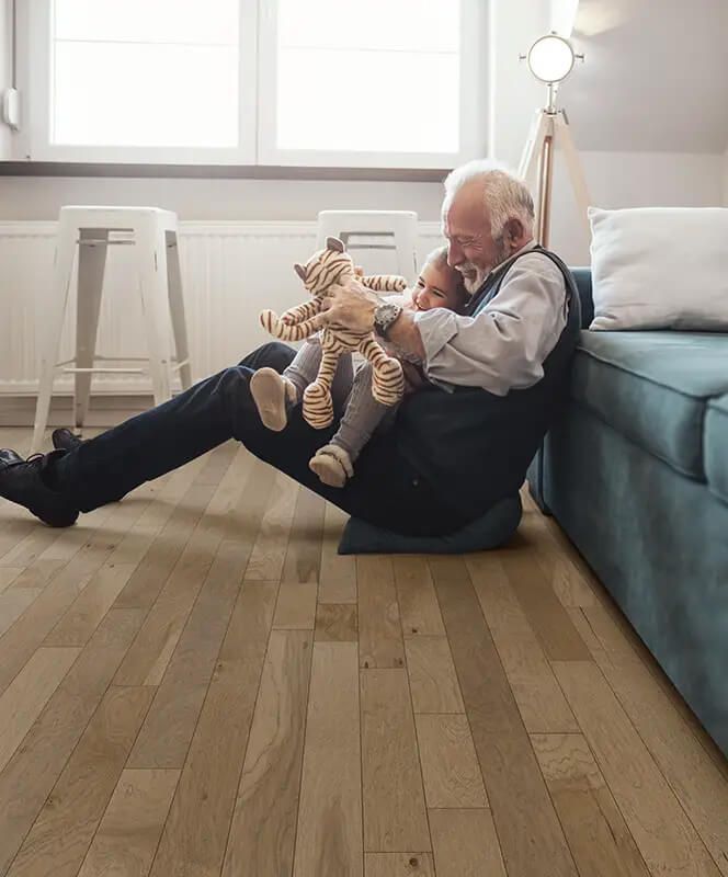 Elderly person and child playing with toys on hardwood floor, near a blue sofa.