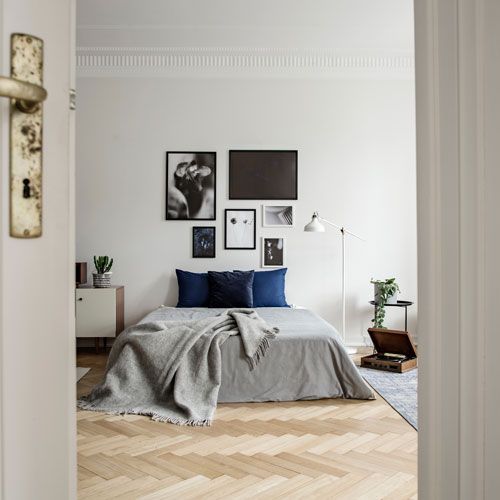 Bedroom interior with grey and blue accents, wooden floor, and art gallery wall.