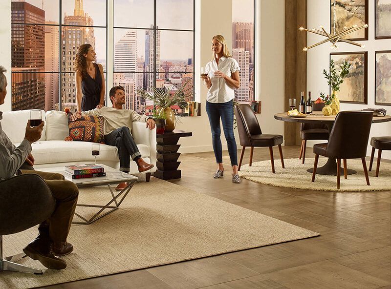 People in a living room with city view, talking, some seated and some standing, with wine.