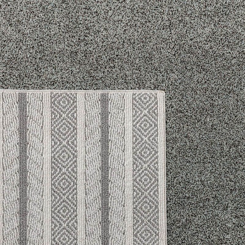 Corner of patterned rug, light gray with diamond and stripe design, next to solid gray carpet.