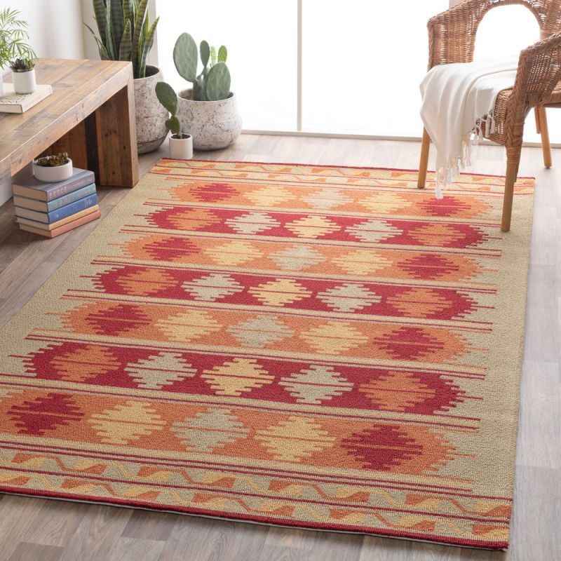 Southwestern-style rug with red, orange, and yellow geometric patterns on a beige background; near a chair and plants.