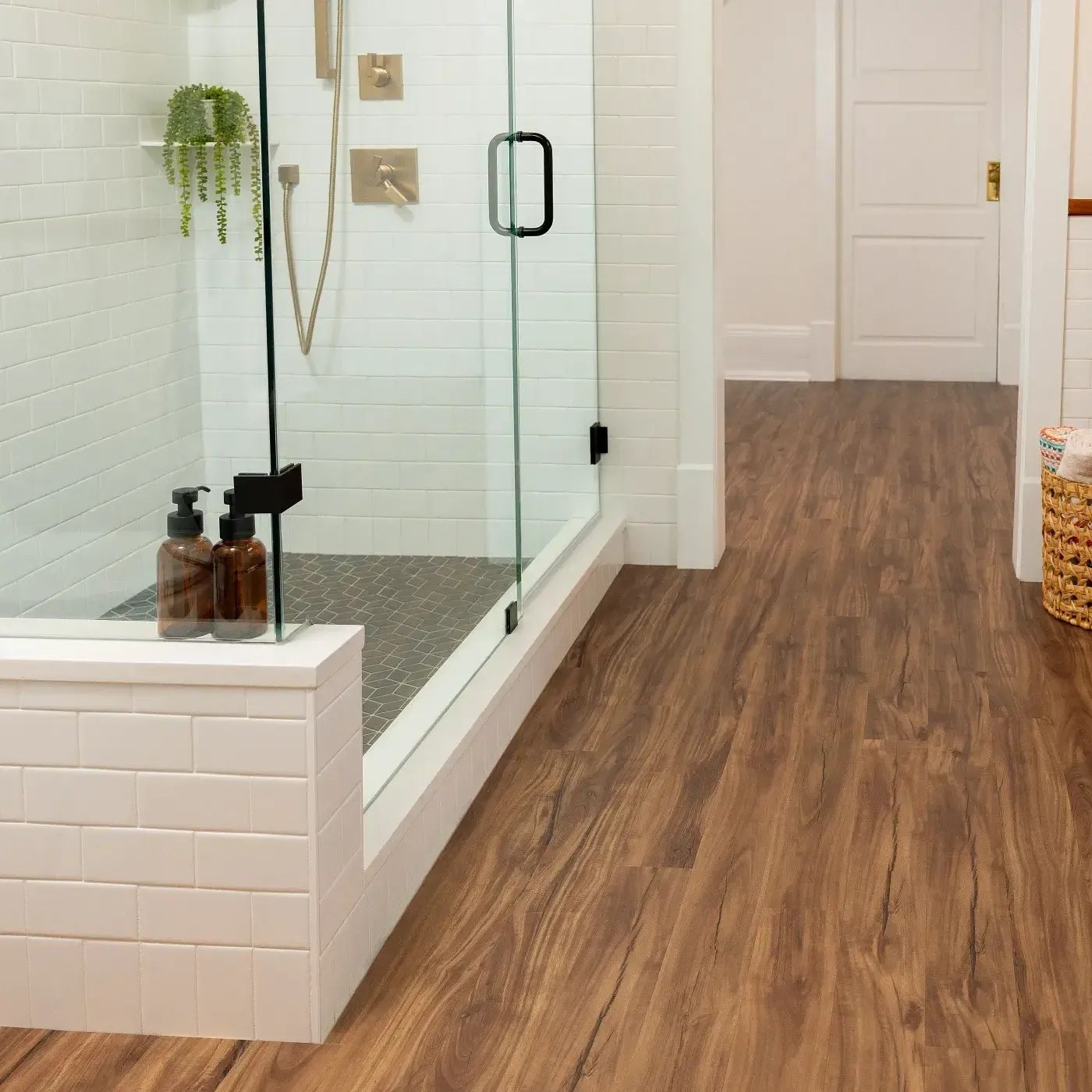 Bathroom with glass shower, white subway tile, and wood-look flooring.