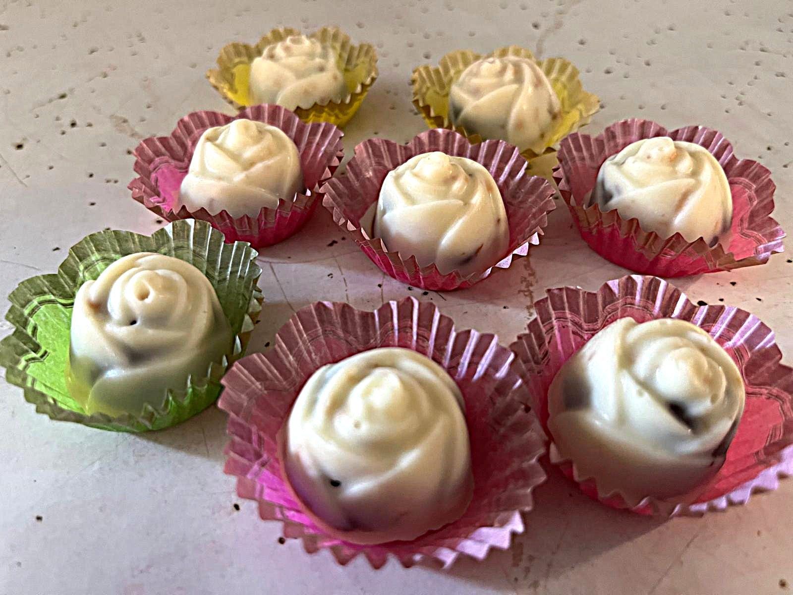 Assorted white frosted candies in pink and green paper cups on a countertop
