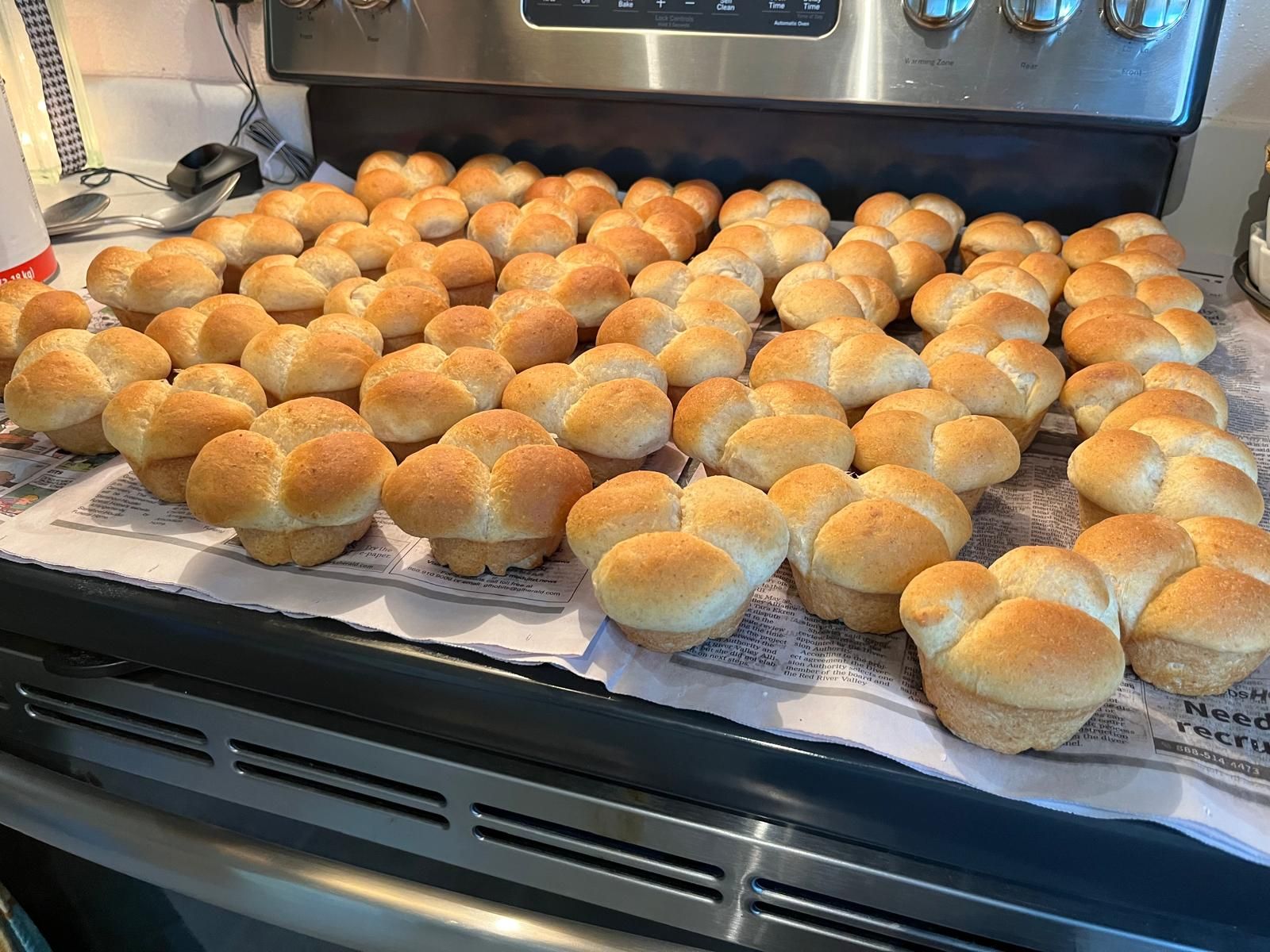 Tray of freshly baked rolls cooling on a stovetop covered with paper towels.