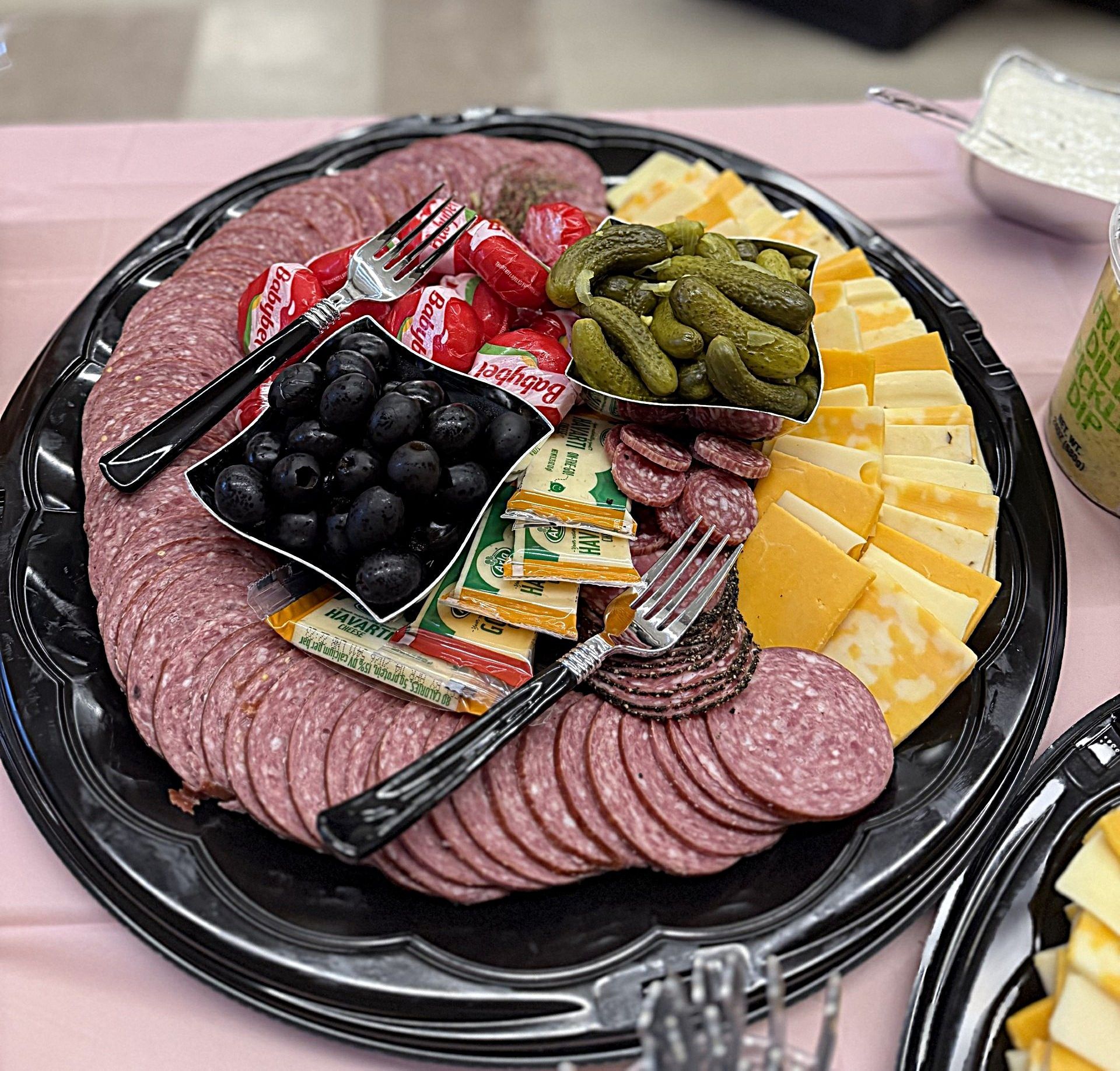 Charcuterie platter with sliced meats, cheeses, olives, berries, pickles, and crackers on a black tray