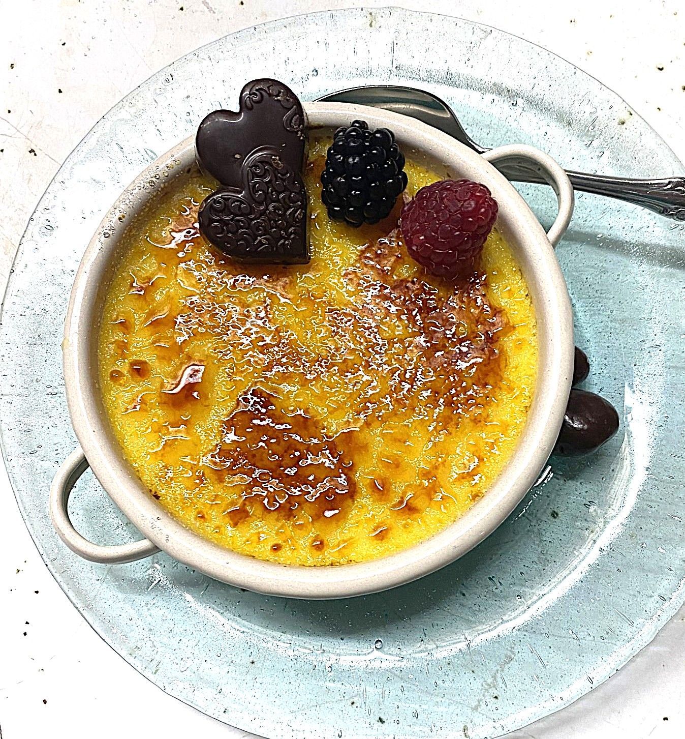 Crème brûlée in a white ramekin with berry garnish on a pale blue plate