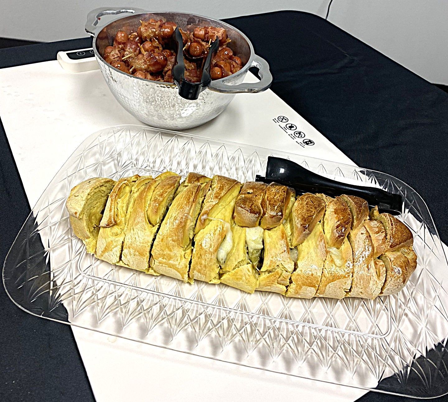 Sliced golden pastry on a tray with a bowl of glazed berries on a dark table
