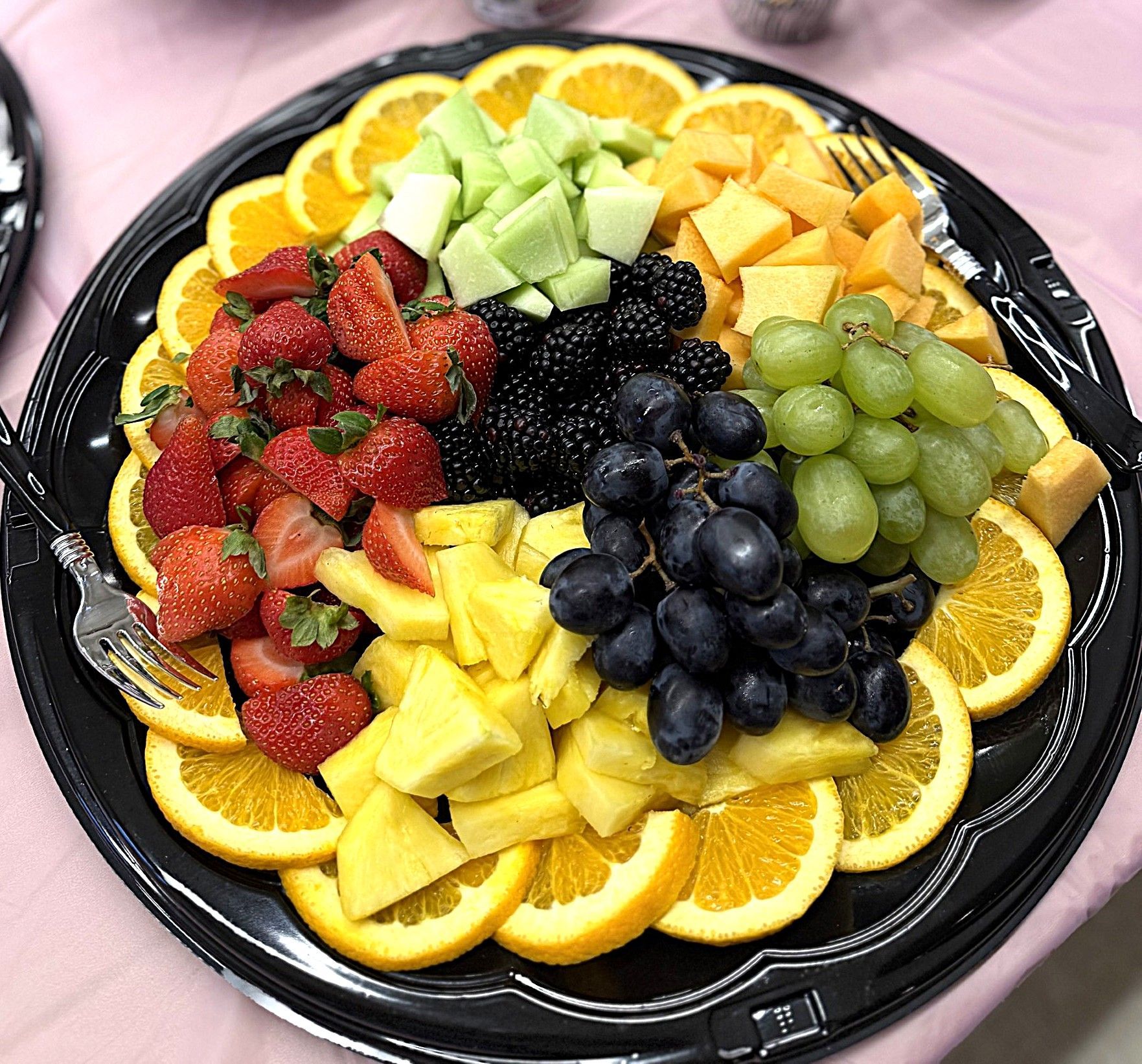 Assorted fruit platter on a black tray with orange slices, strawberries, grapes, kiwi, mango, and blueberries