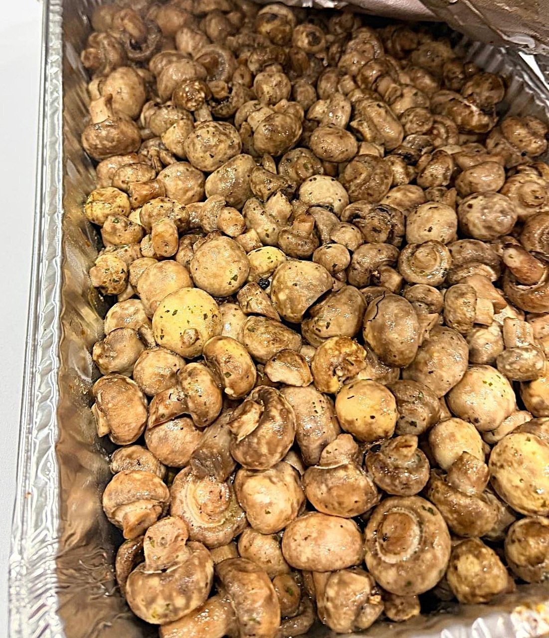 Tray filled with small brown mushrooms, some dusted with seasoning or soil.