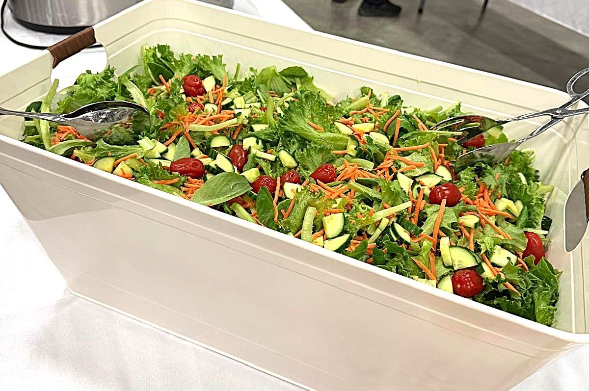 Large white tray of mixed green salad with cherry tomatoes and a serving spoon