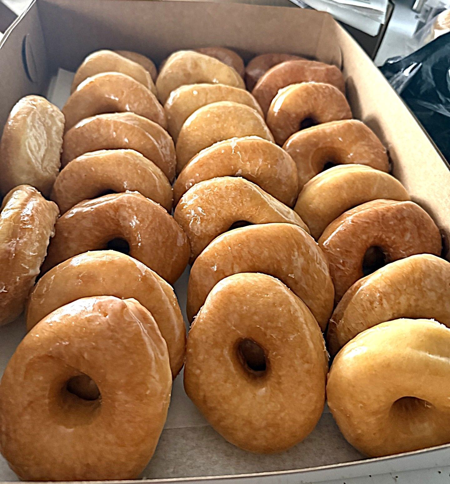 Box of glazed donuts, neatly arranged in rows with golden-brown tops and one lighter donut in front