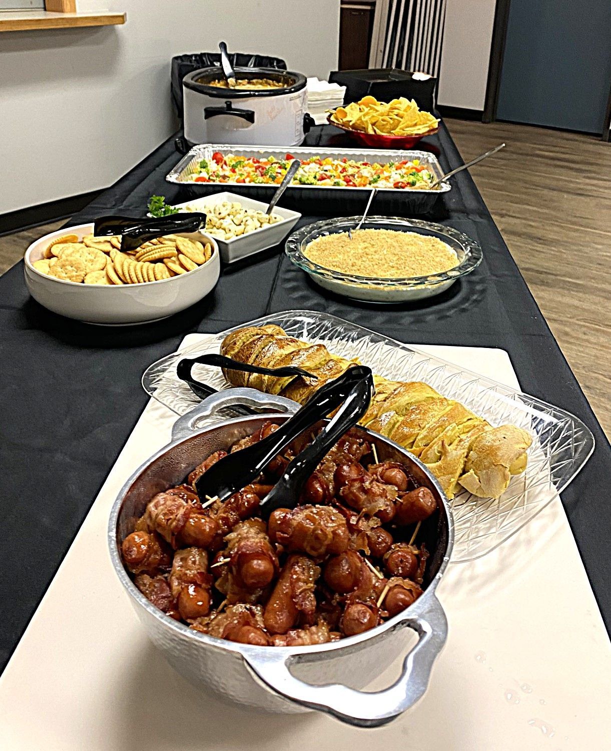 Buffet table with various dishes, including glazed meat, salad, noodles, and other appetizers on black tablecloth