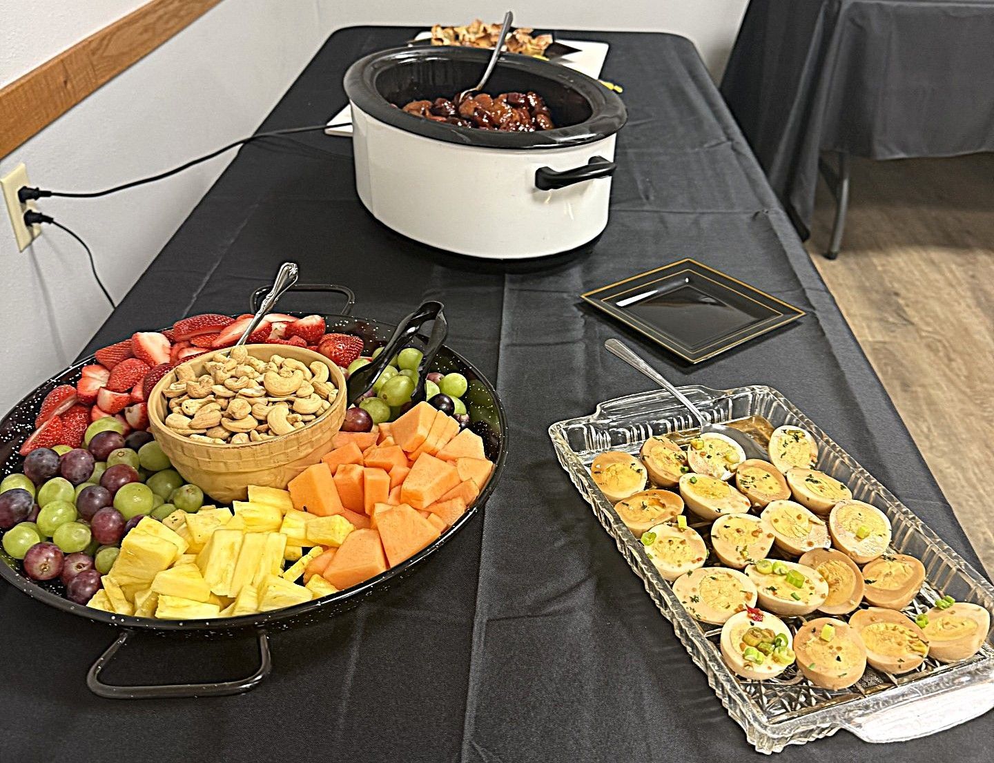 Buffet table with fruit platter, cheese cubes, deviled eggs, and a crockpot of hot food