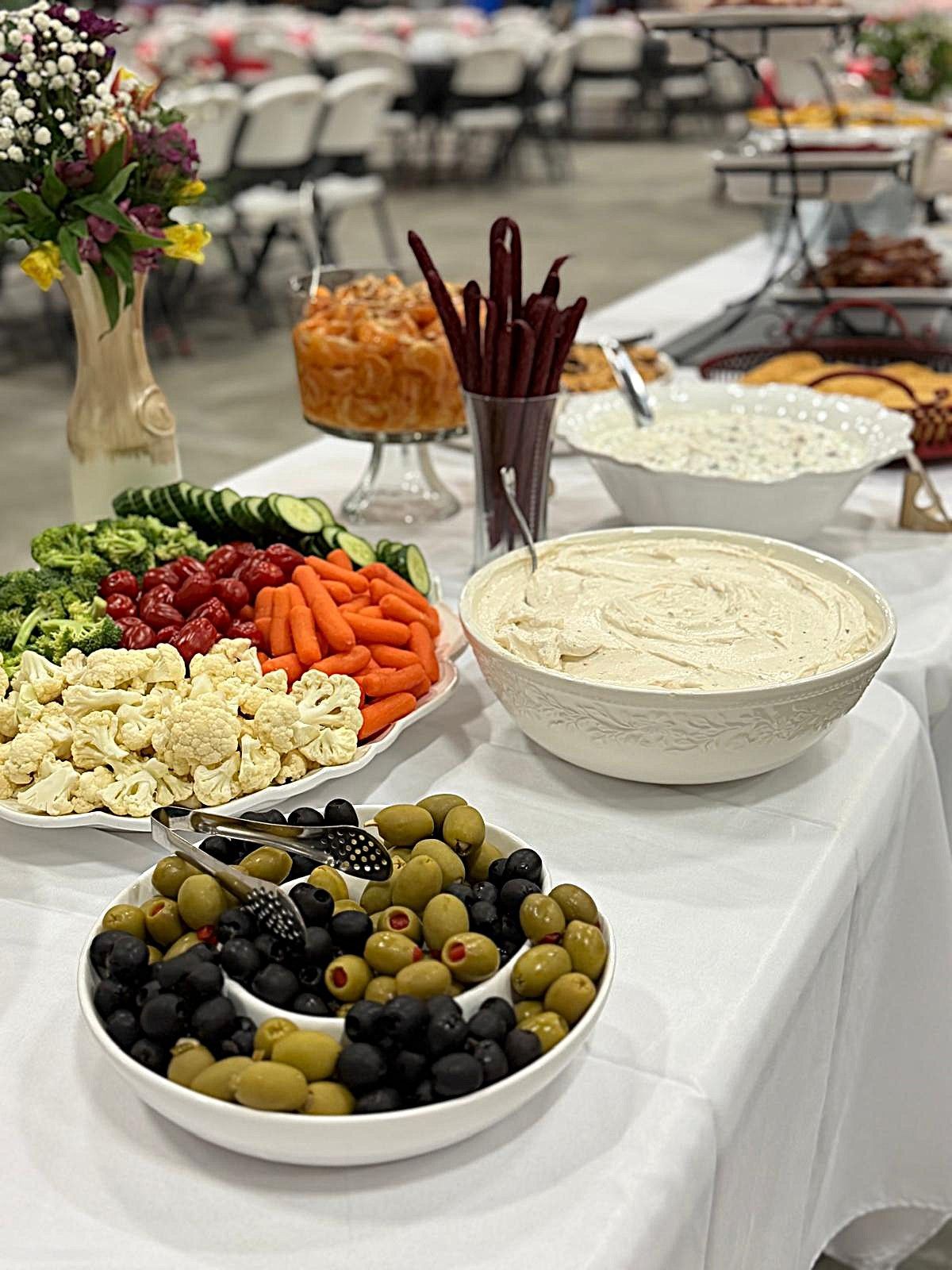 Buffet table with fresh vegetables, olives, dips, breadsticks, and bowls of salad and hummus