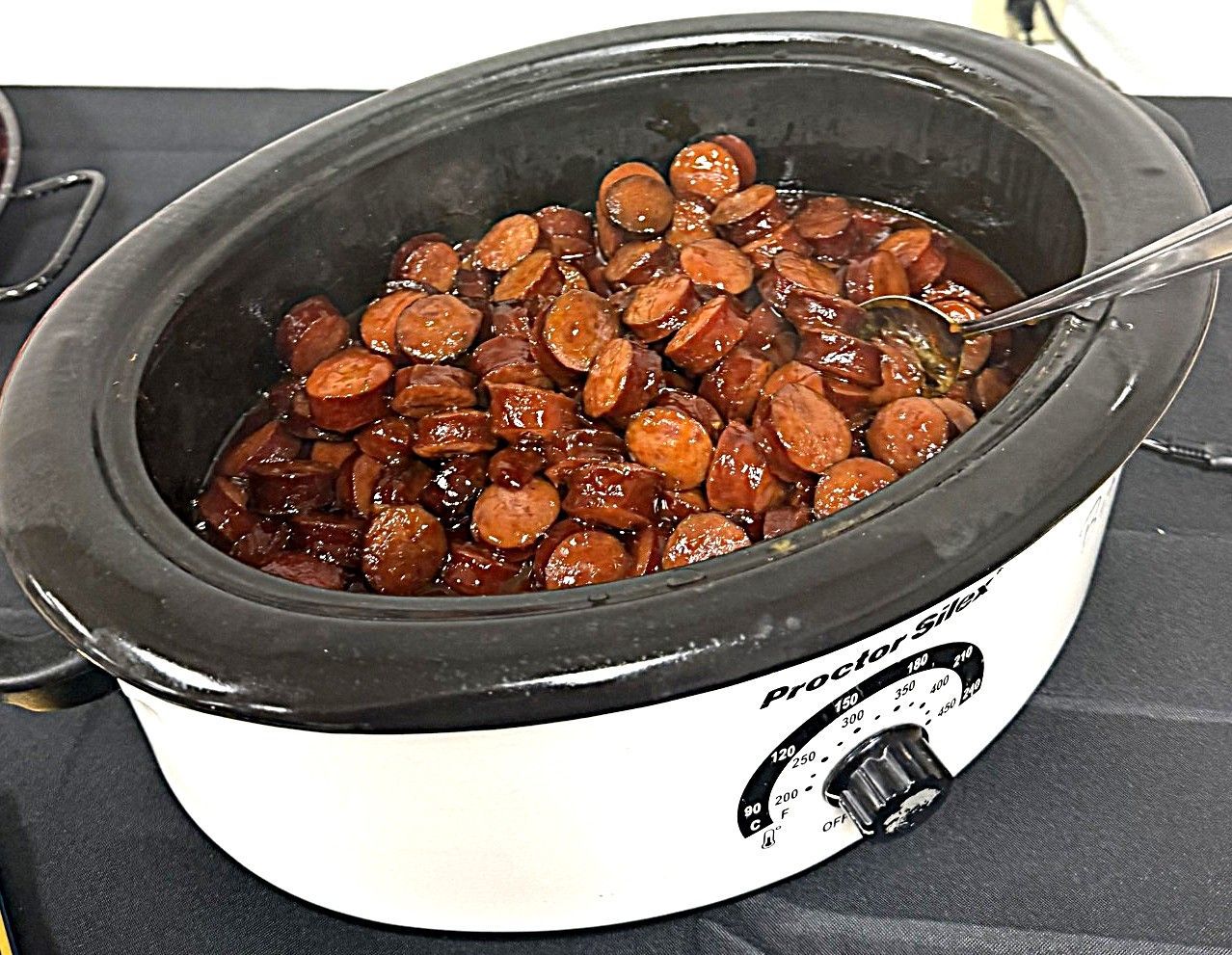 Slow cooker filled with glazed sausage slices, with a serving spoon inside.