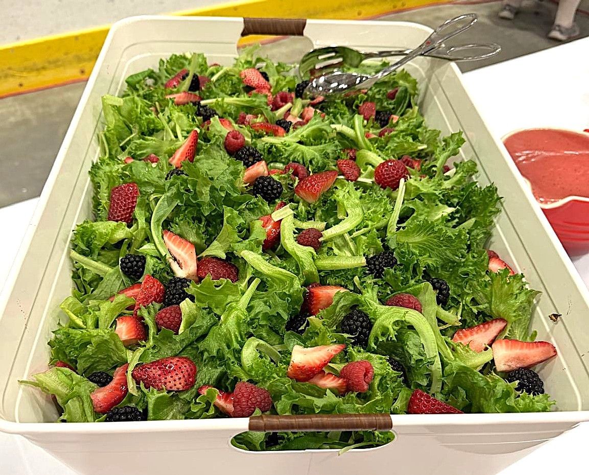 Large tray of green salad topped with sliced strawberries on a table