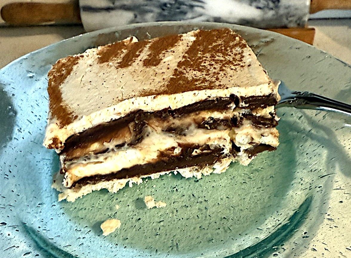 Slice of tiramisu dusted with cocoa on a green plate, with a fork beside it.
