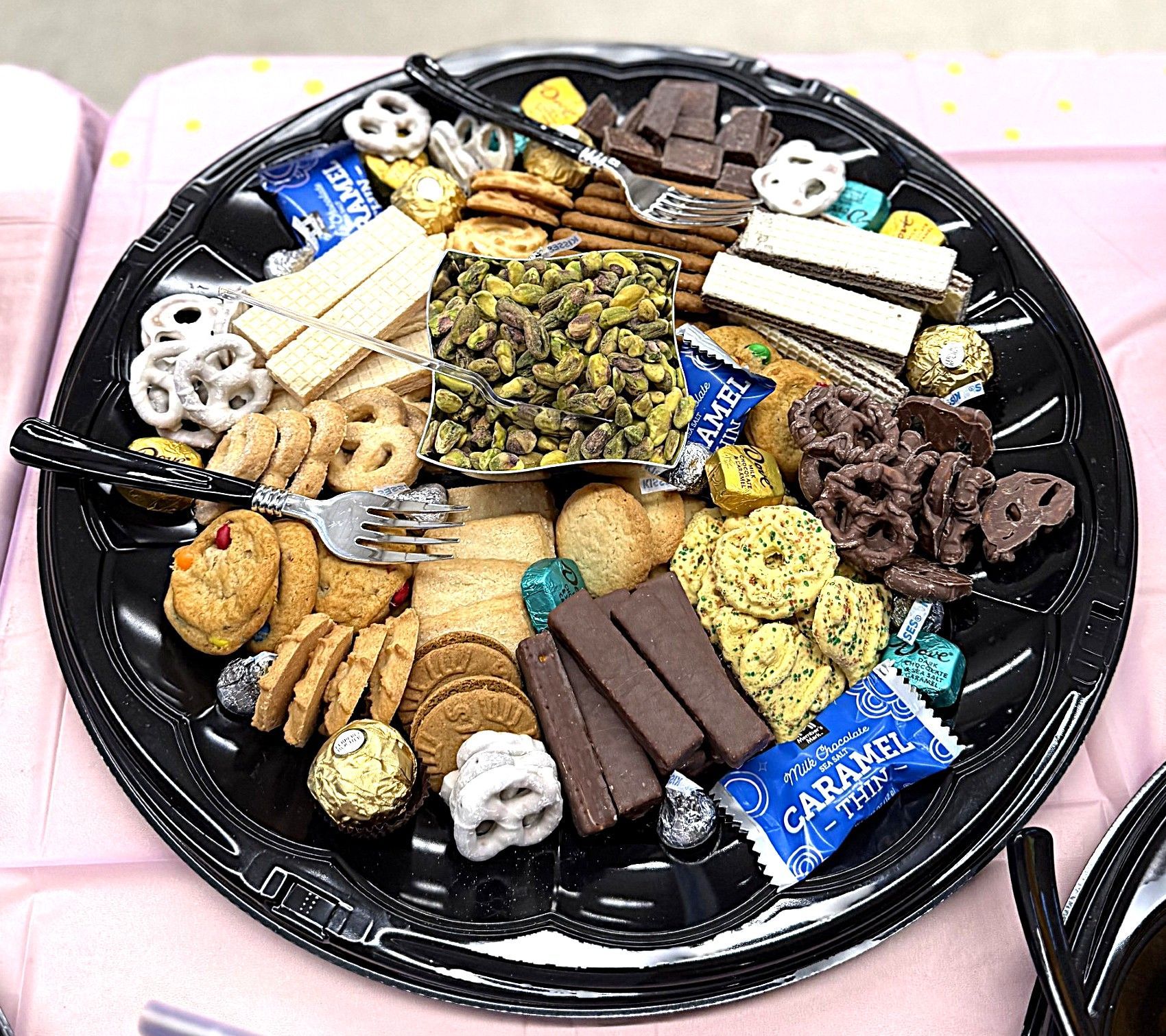 Assorted chocolates and cookies arranged on a black tray with pink tablecloth underneath
