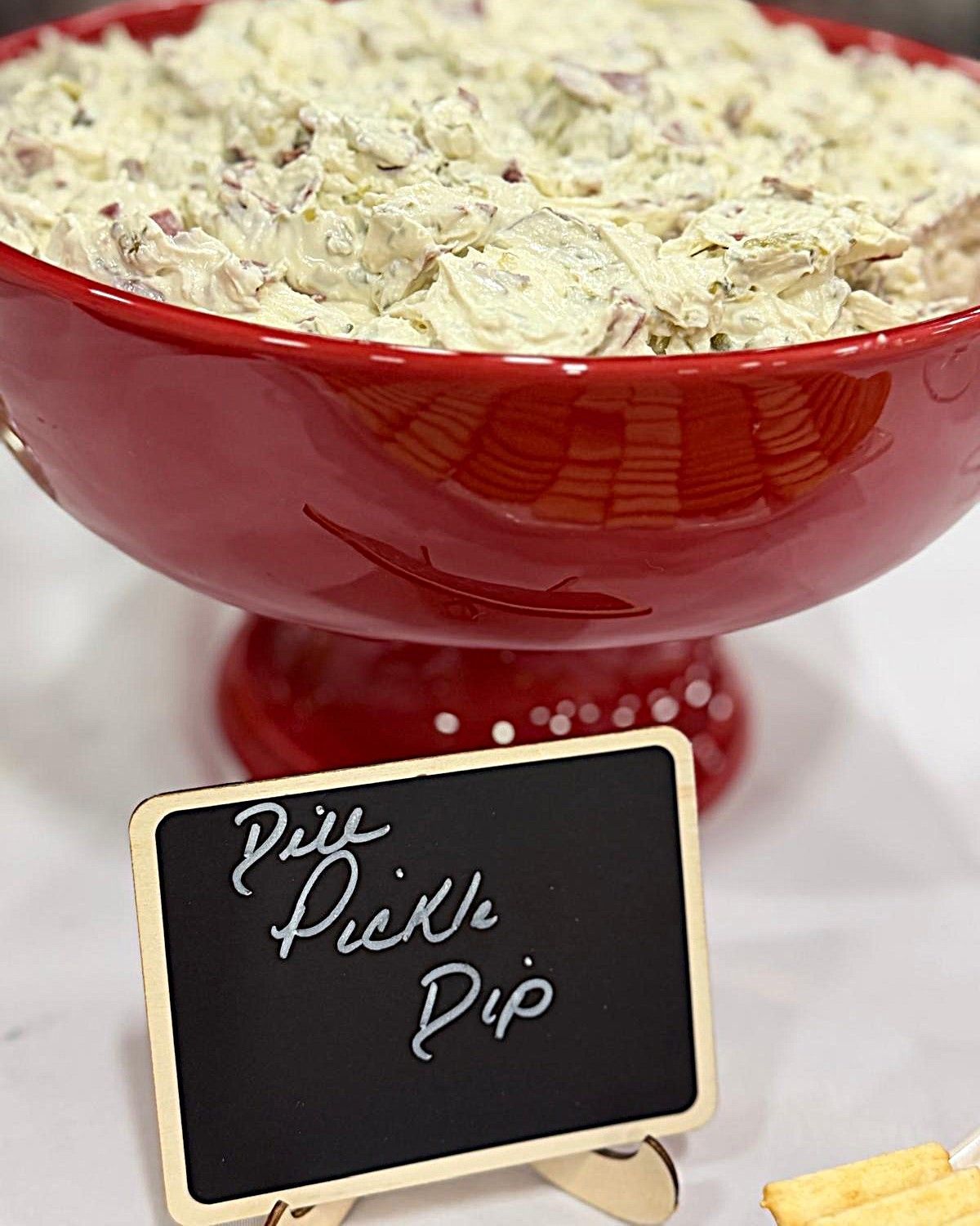 Red bowl of creamy dip with a chalkboard label reading “Piz Pickle Dip”