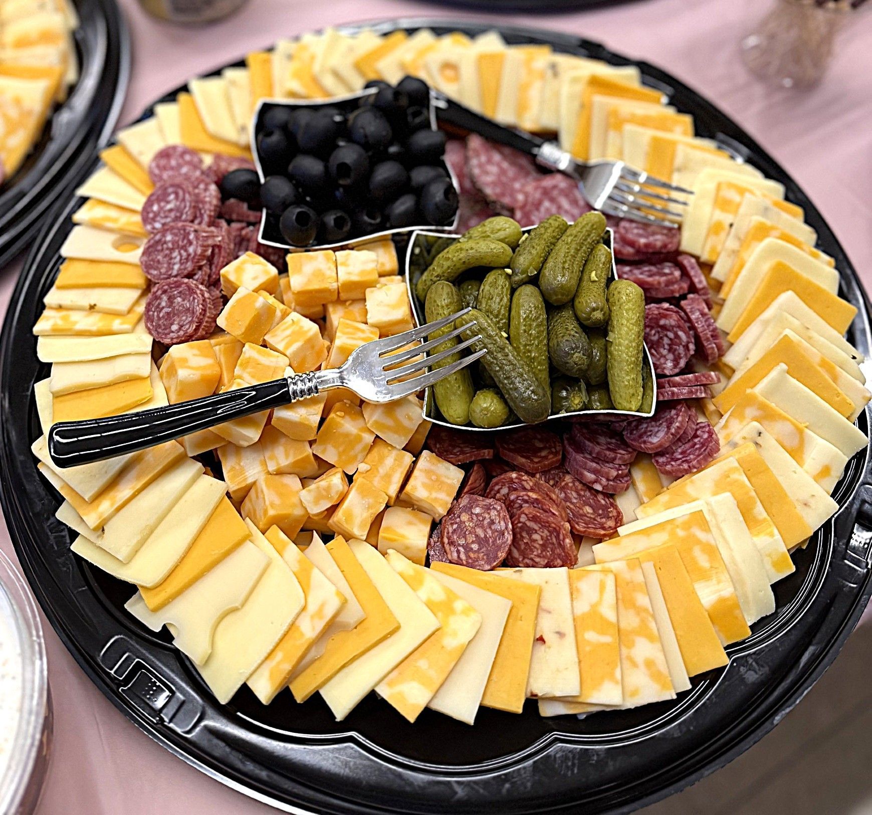 Assorted cheeses, olives, pickles, and cured meats arranged on a round black platter with a serving fork