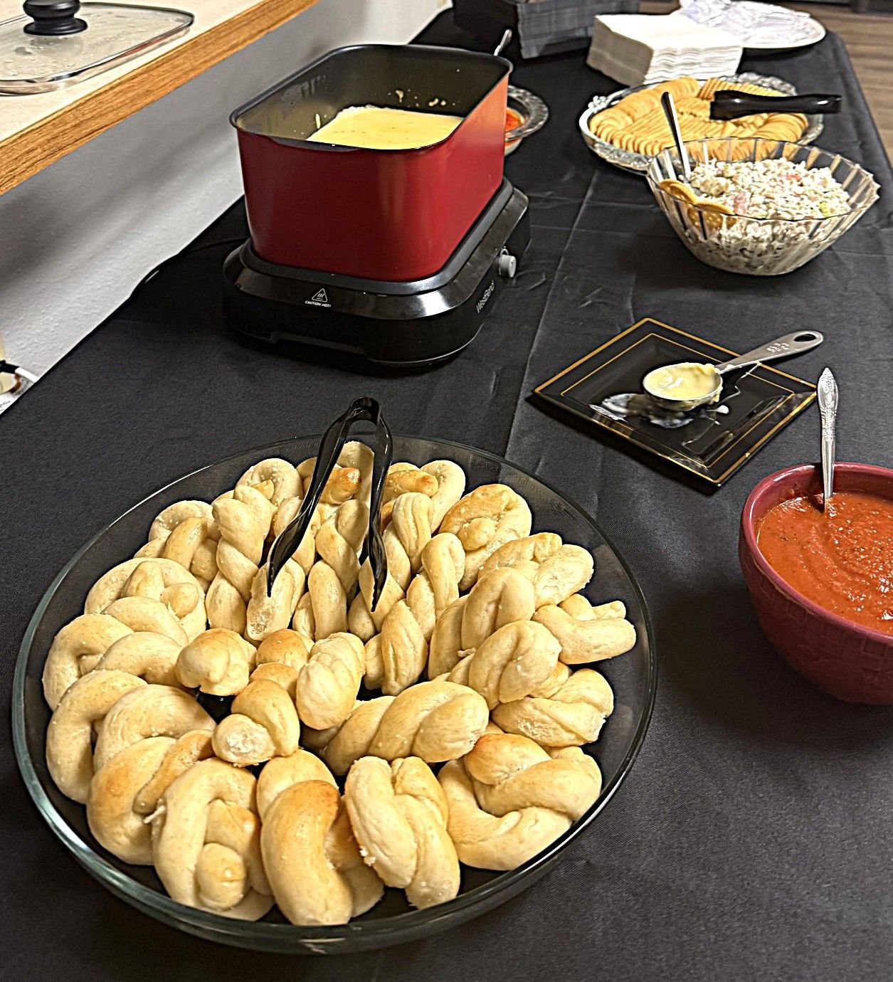 Buffet table with bread rolls, red sauce, and cheese fondue in a red pot