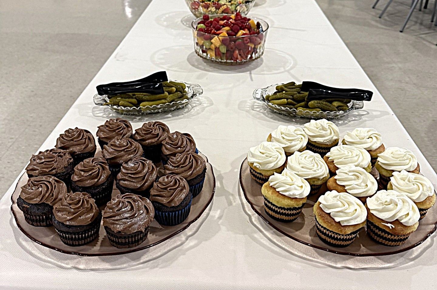Dessert table with trays of chocolate and vanilla cupcakes and a bowl of fruit in the center