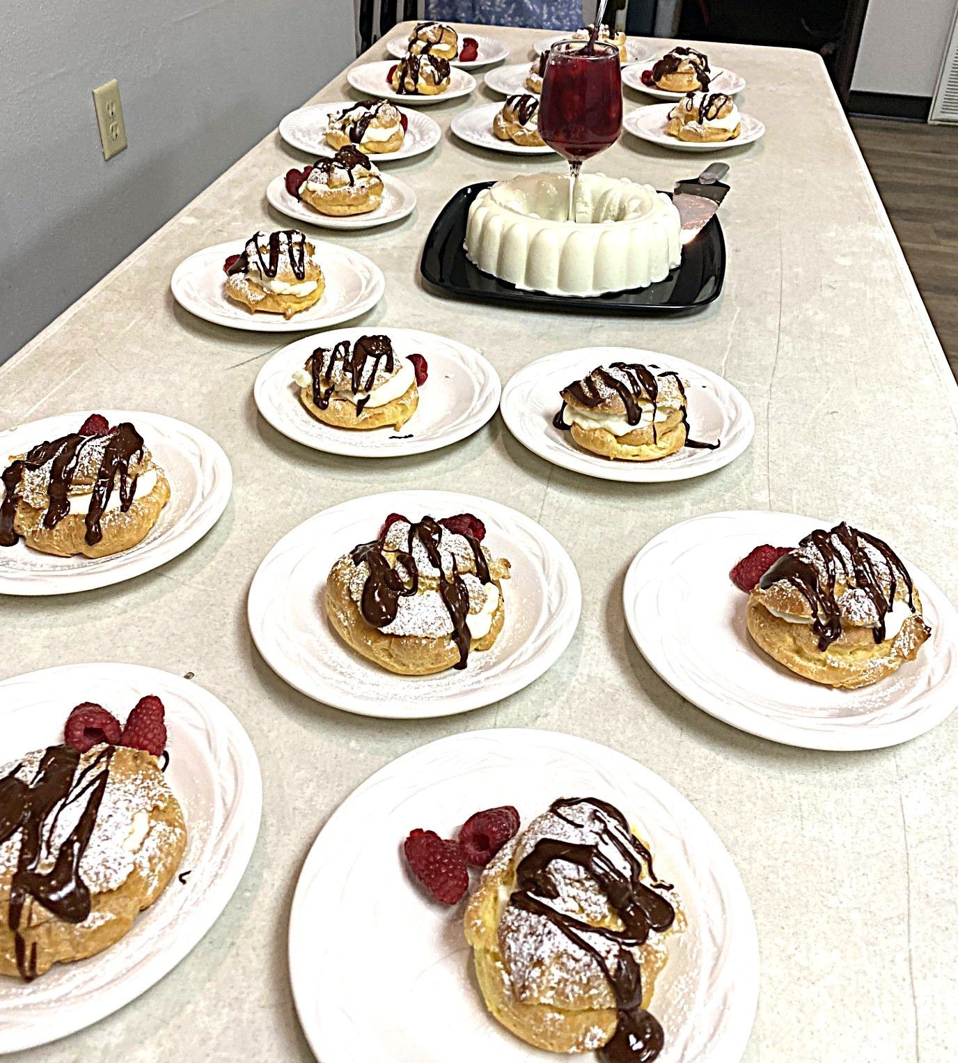 Dessert table with plated pastries, whipped cream, chocolate drizzle, and a white bundt cake centerpiece