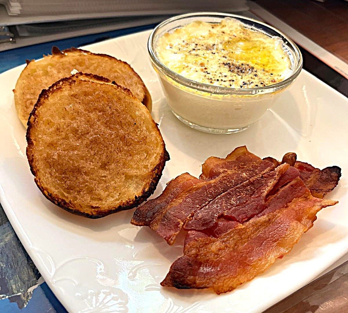 Breakfast plate with toast, a small dish of eggs, and crispy bacon