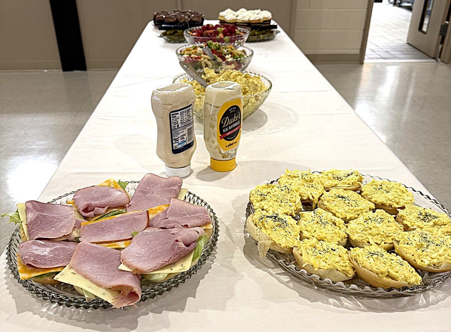 Table of assorted sandwiches and desserts with condiments in a cafeteria-style setting