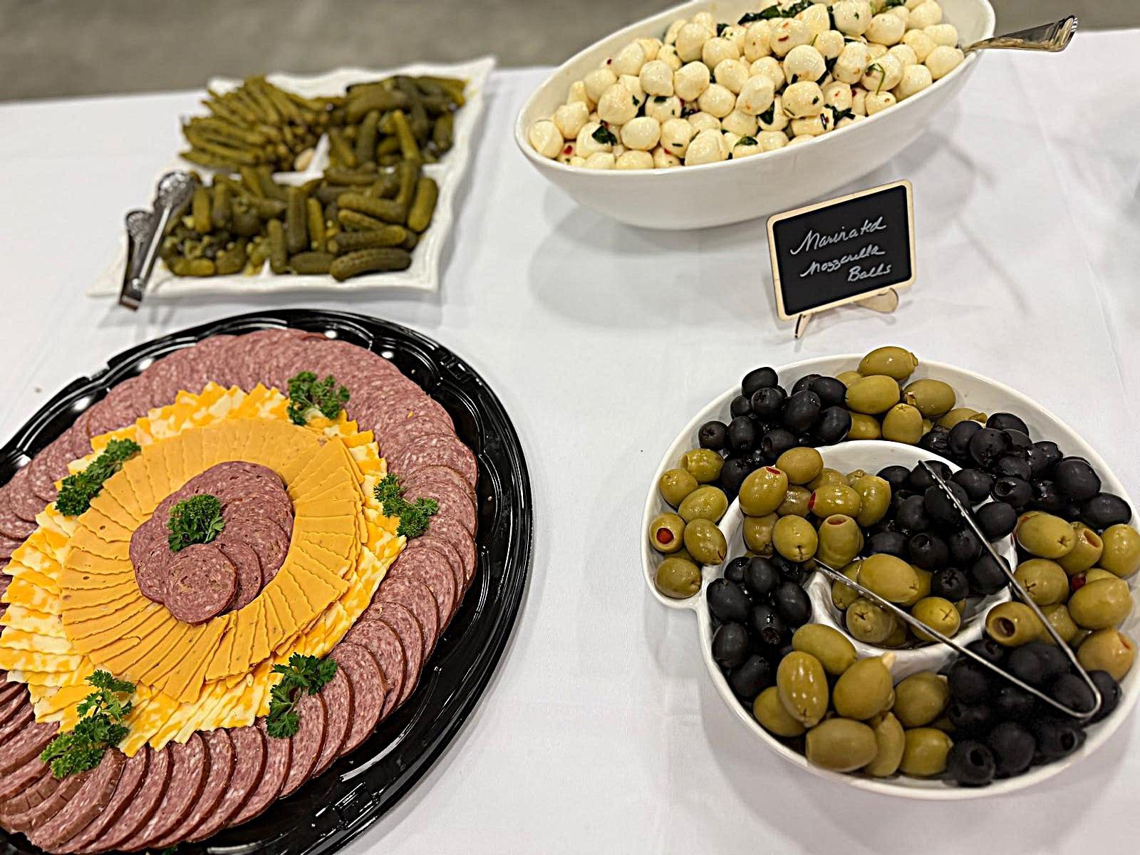 Buffet table with assorted olives, pickles, and a sunflower-shaped platter of sliced meats and cheese.