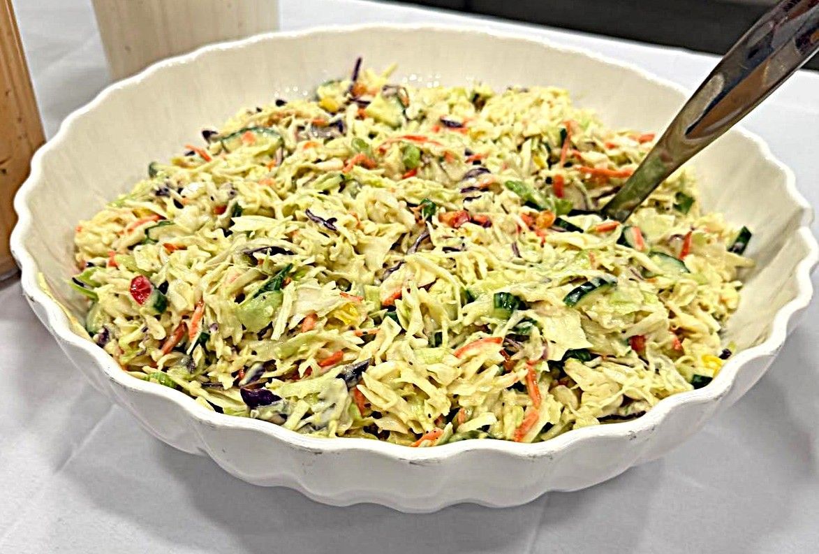 Bowl of creamy vegetable salad with shredded carrots and herbs, served with a spoon