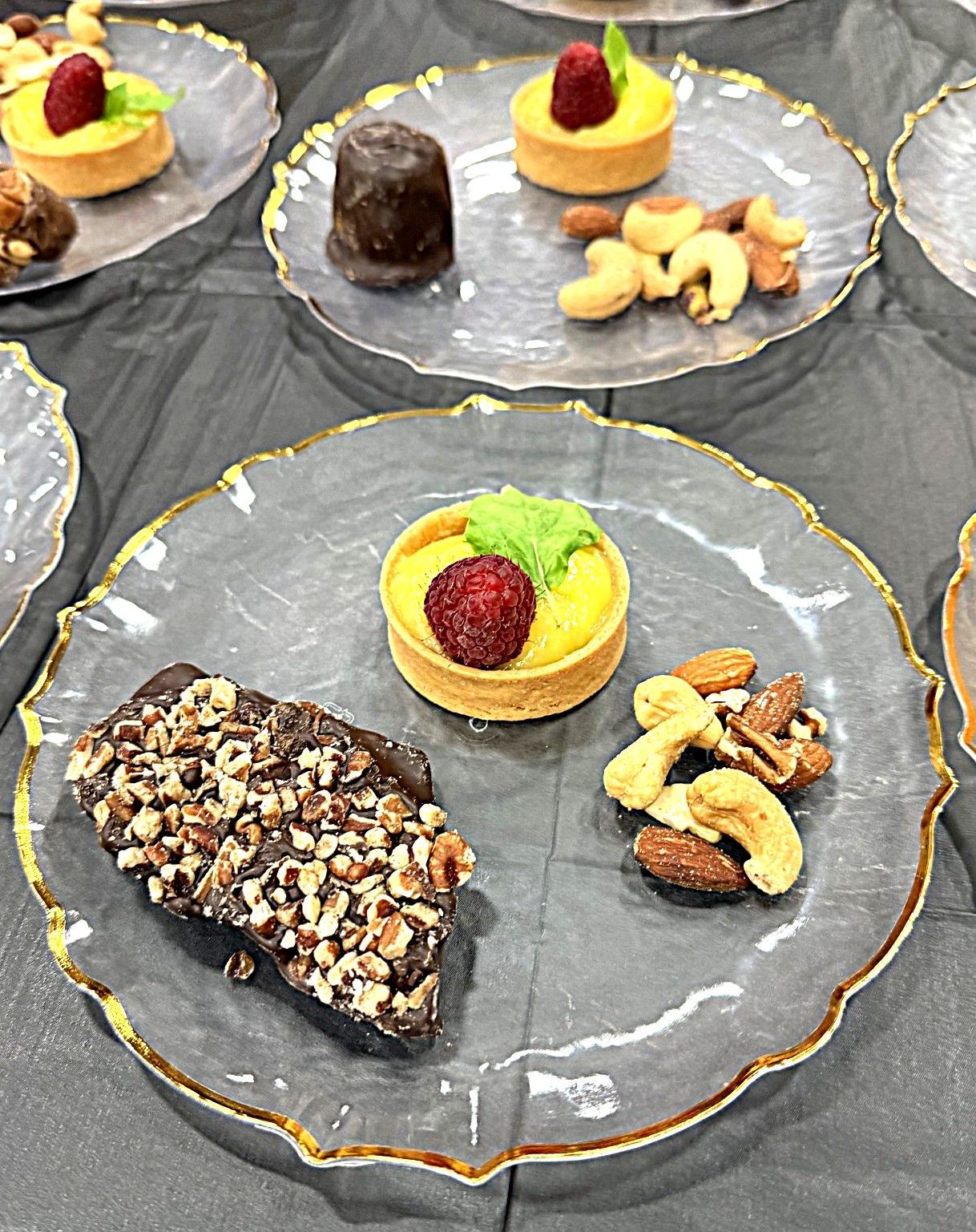 Assorted pastries and nuts on clear glass plates with gold-trimmed edges, arranged on a dark tablecloth