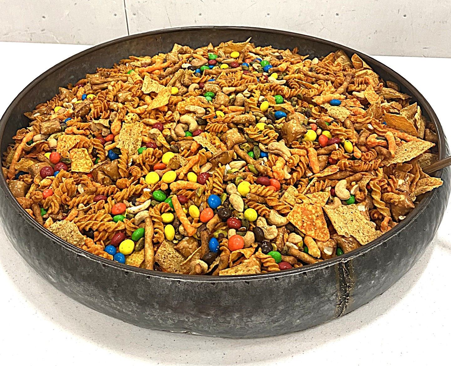 Shallow black pan filled with trail mix, cereal, nuts, and colorful candy-coated chocolates