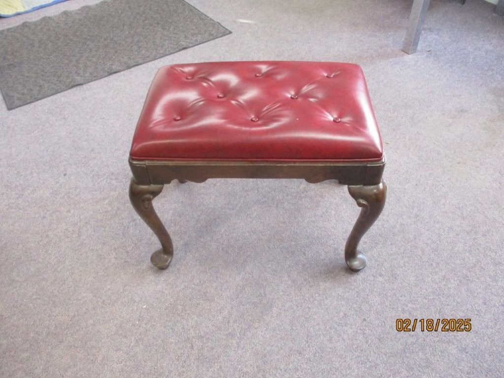 Red leather tufted ottoman with dark wood legs on a light carpeted floor.
